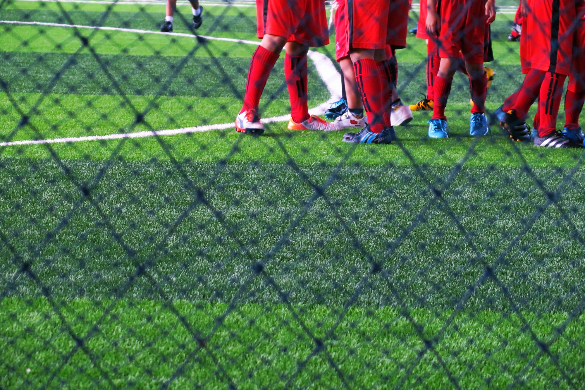 soccer-team-player-wearing-red-sport-suit-standing-in-green-field-indoor-stadium-closeup-background.jpg